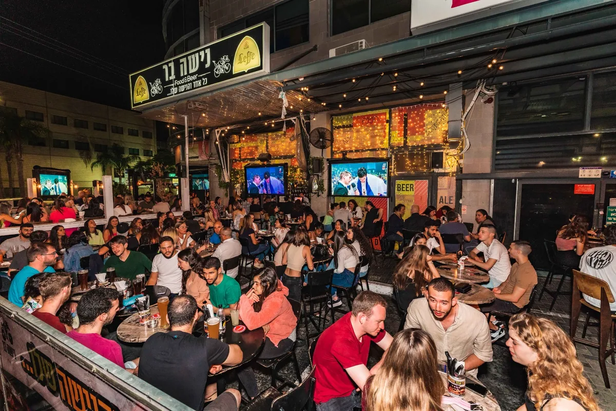 החצר המלאה של נישה בר בערב, מתחת לשלט ולשרשראות התאורה
